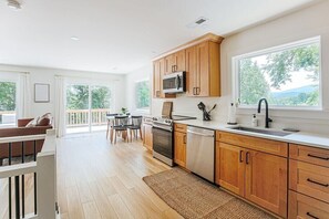 Een moderne keuken met houten kastjes, roestvrijstalen apparatuur en een groot raam met uitzicht op groen.
