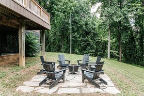 An outdoor seating area with Adirondack chairs and a fire pit, surrounded by a stone patio and a wooden deck. - Fox Hill: Hot Tub, Views, Pet Friendly! (Afton)
