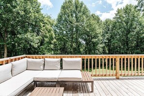 A wooden deck with a built-in sofa and table, surrounded by dense trees.