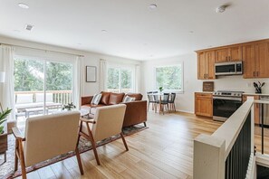 A spacious living area with a brown leather sofa, a dining table with chairs, and a kitchen with wooden cabinets and a microwave. - Fox Hill: Hot Tub, Views, Pet Friendly! (Afton)