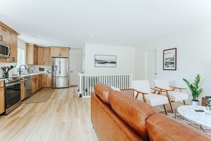 A modern kitchen with wooden cabinets, stainless steel appliances, and a dining area with a leather sofa and white chairs.