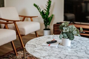 A modern living room with a round marble coffee table, a remote control, a book, and a potted plant. - Fox Hill: Hot Tub, Views, Pet Friendly! (Afton)
