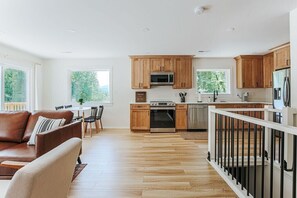 A modern kitchen with wooden cabinets, a stainless steel refrigerator, and a dining area with a leather sofa and dining table.