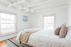 Ein helles Schlafzimmer mit einem großen Bett, zwei Fenstern und einem Bild an der Wand.