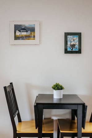 Un coin repas avec une table et des chaises, une petite plante en pot et deux œuvres d’art encadrées accrochées au mur.