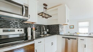 A modern kitchen with white cabinets, a stainless steel dishwasher, and a black tiled backsplash. - Green on New - Central Location and Staunton Charm (Staunton)