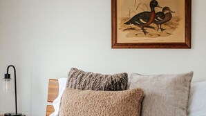A neatly made bed with two pillows and a blanket, a framed picture of birds on the wall, and a bedside table with a lamp. - Green on New - Central Location and Staunton Charm (Staunton)