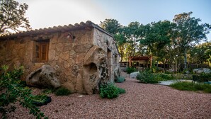 Un bâtiment rustique en pierre, doté d’une porte et d’une fenêtre en bois, entouré d’un chemin de gravier et de verdure.