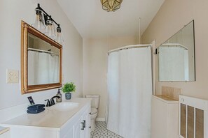 Een badkamer met een wit wastafelmeubel, een spiegel met houten lijst, een douchegordijn en een radiator.
