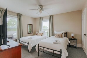 Een slaapkamer met twee bedden, een plafondventilator, een televisie en een bureau.