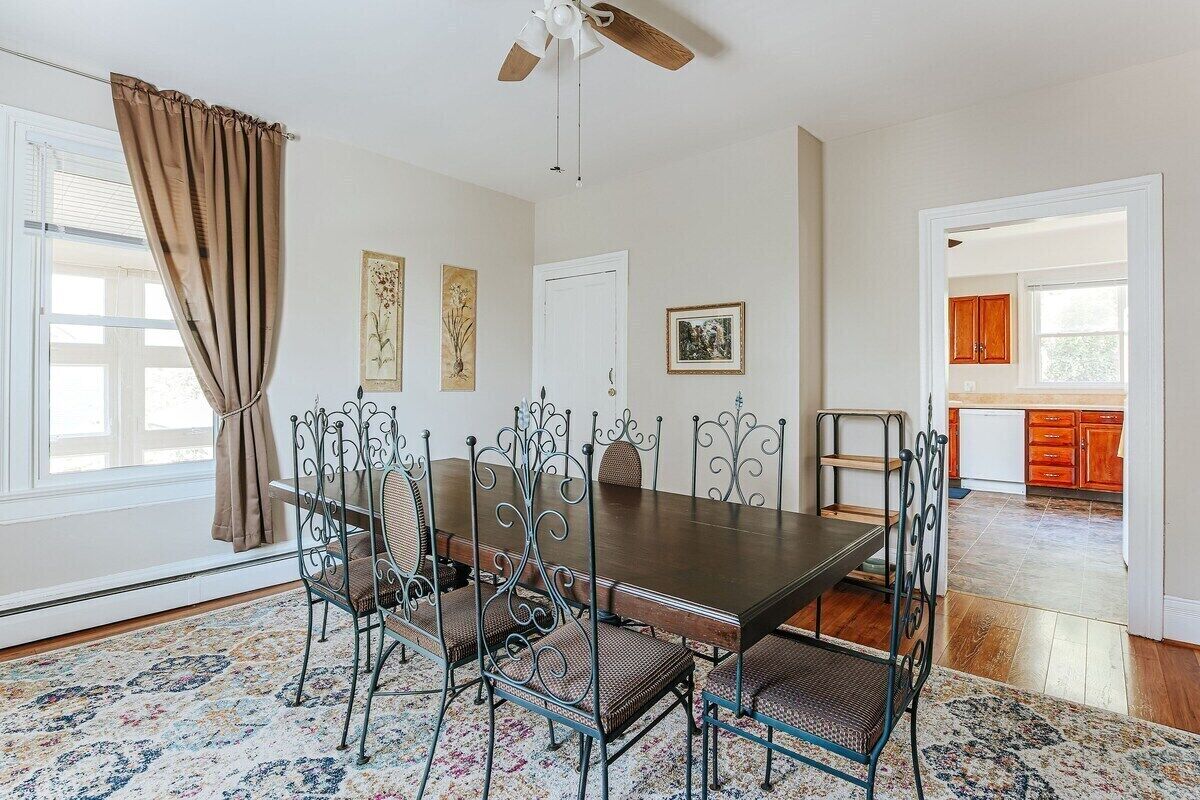 A dining room with a dark wooden table and metal chairs, a ceiling fan, and a view into the kitchen.