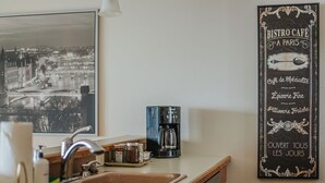 A kitchen with a coffee maker, a sink, and a framed black and white photo of a cityscape. - Panoramic Peak: Wintergreen Condo with Views (Wintergreen Resort)