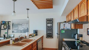 A modern kitchen with wooden cabinets, a black refrigerator, a stove, and a large window with a cityscape view. - Panoramic Peak: Wintergreen Condo with Views (Wintergreen Resort)