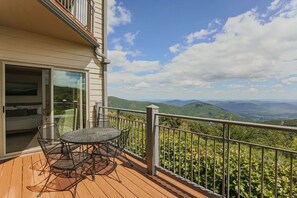 Un balcon avec une table et des chaises, offrant une vue sur des collines verdoyantes et des montagnes.