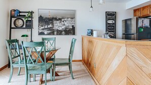 A modern kitchen with a wooden island, a dining area with green chairs, a black and white cityscape photo, and a chalkboard menu. - Panoramic Peak: Wintergreen Condo with Views (Wintergreen Resort)