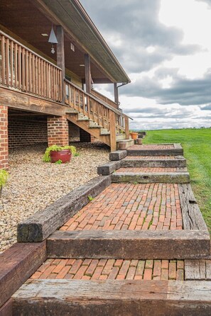 A wooden porch with steps leading to a brick entrance, surrounded by gravel and potted plants.