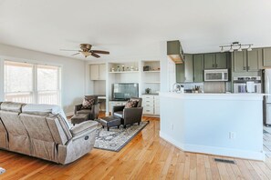 A modern living room with a sofa and ottoman, a television, and a kitchen with green cabinets and white appliances. - Ridgeview Retreat: Mountain Views and Pet Friendly (Staunton)