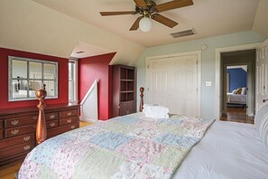 A bedroom with a large bed, a wooden dresser, a ceiling fan, and a staircase leading to another room.