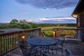 A wooden deck with a round table and chairs, overlooking a grassy landscape and trees. - Ridgeview Retreat: Mountain Views and Pet Friendly (Staunton)