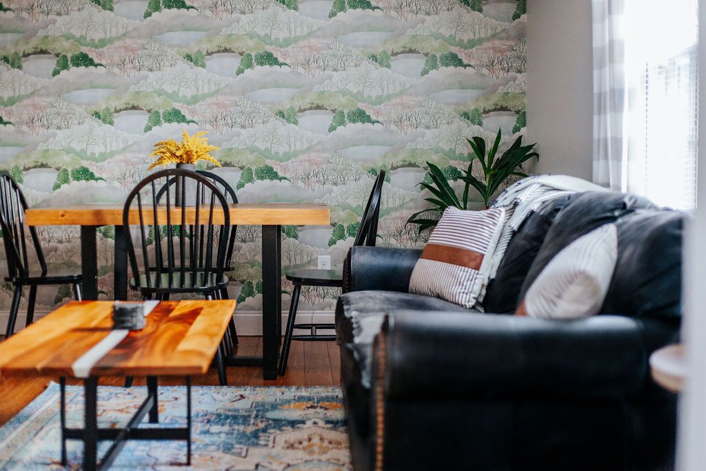 Ein Wohnzimmer mit einem Holzesstisch, schwarzen Stühlen, einem schwarzen Ledersofa und einem gemusterten Teppich.