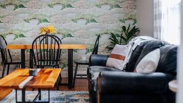 Ein Wohnzimmer mit einem Holzesstisch, schwarzen Stühlen, einem schwarzen Ledersofa und einem gemusterten Teppich.