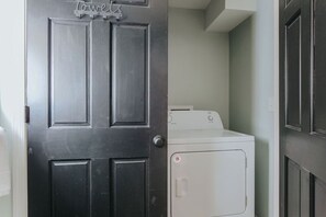 Un cuarto de lavandería con una puerta negra, una secadora blanca y un ventanal pequeño.