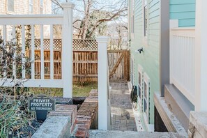 A private property with a gated entrance, a wooden fence, and a brick pathway leading to a house with light green siding.