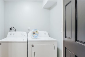 A laundry room with two white washing machines and a Tide detergent bottle on one.