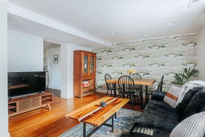 Un salon comprenant un téléviseur, un meuble de rangement en bois, une table à manger avec des chaises et un canapé.