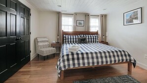 Una camera da letto con copriletto a scacchi, una testiera in legno, una sedia, un comodino e un quadro appeso al muro.