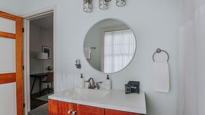A bathroom with a white sink, wooden vanity, round mirror, and a towel ring. - The Landmark: Luxury In Downtown Staunton (Staunton)
