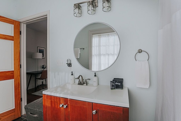 Une salle de bain avec un lavabo blanc, un meuble-lavabo en bois, un miroir rond et un porte-serviette.