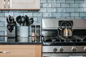 Una cocina con estufa de acero inoxidable, hervidor y especiero con diferentes especias.