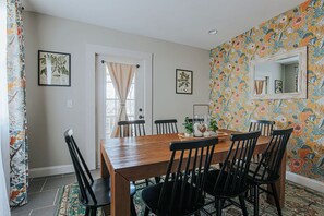 Un coin repas avec une table en bois et des chaises noires, un papier peint à motifs floraux et un miroir au mur.