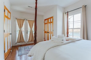 A bedroom with a four-poster bed, a large window with curtains, and a wooden door.