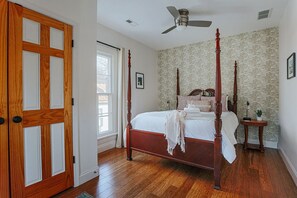 Une chambre à coucher avec un lit à baldaquin, un plancher en bois, un ventilateur de plafond et une fenêtre avec des rideaux.