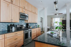 Une cuisine moderne avec des meubles en bois, un four à micro-ondes en acier inoxydable, une cuisinière à gaz et un plan de travail noir.