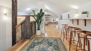 A modern kitchen with wooden flooring, a bar area with stools, and a staircase with a rustic finish.