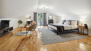 A spacious loft bedroom with a large bed, a desk, a chair, and a TV.