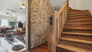 A wooden staircase leading to a loft area with exposed brick walls and a modern kitchen in the background.