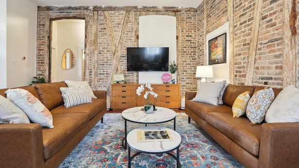 A living room with two brown leather sofas, a round coffee table, and a large flat-screen TV mounted on a brick wall.