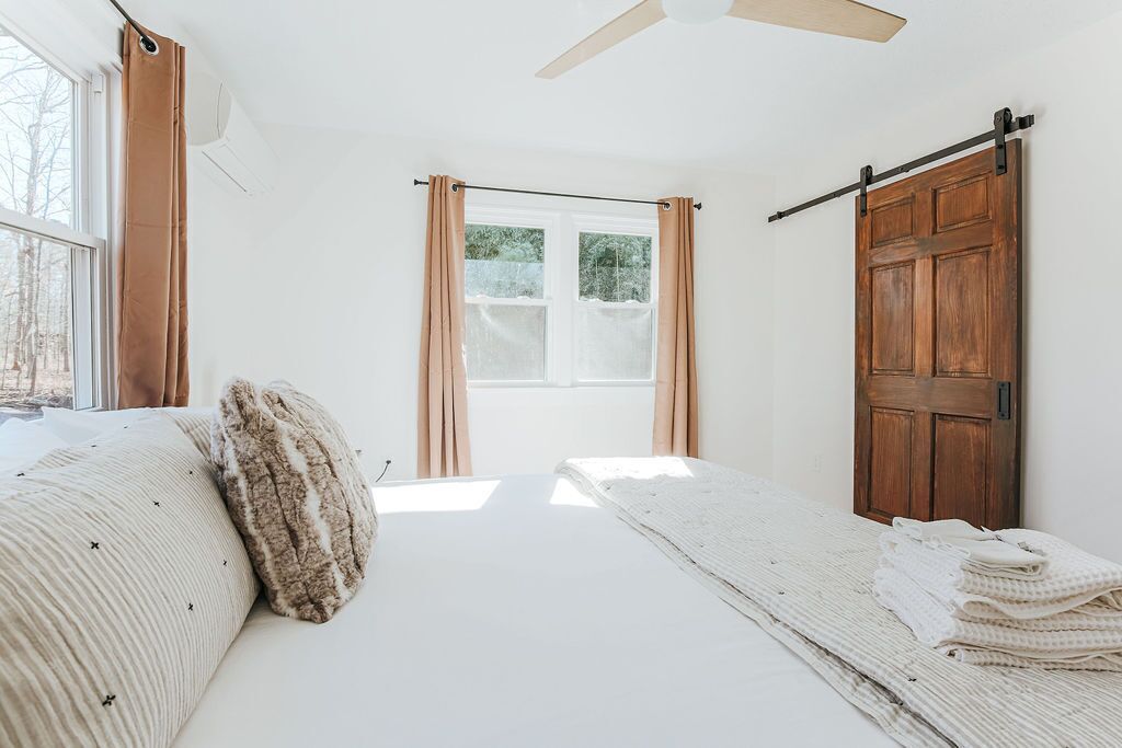 A bedroom with a bed, a window with curtains, a wooden door, and a ceiling fan.