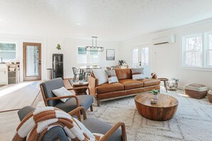 A spacious living room with a brown leather sofa, a wooden coffee table, and a dining area with a table and chairs.