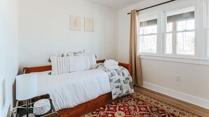 Et soveværelse med seng, et natbord, en lampe, et vindue med gardiner og en tæppe med mønster.