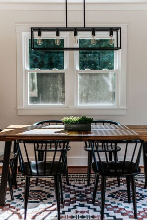 A dining area with a wooden table, black chairs, a black chandelier, and a window with frosted glass panes.