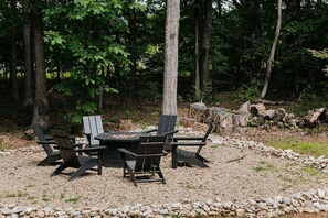 Un espace extérieur aménagé avec une table ronde et quatre chaises Adirondack, entouré d’un chemin de gravier et d’arbres.