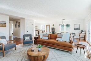 Un salón espacioso con un sofá de cuero marrón, sillones azules y una mesa de centro de madera.
