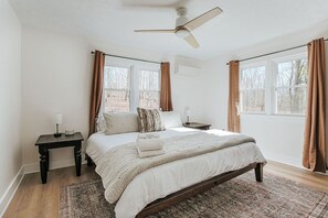 Un dormitorio con una cama, una mesita de noche, un ventilador de techo y dos ventanas con cortinas.