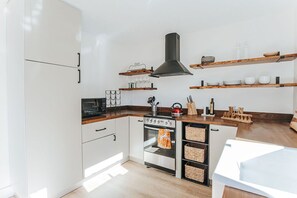 Cozinha moderna com armários brancos, exaustor preto, prateleiras de madeira e forno embutido.
