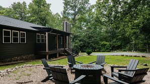 En uteplats med Adirondack-stolar och en eldstad, omgiven av ett område med grus och en träaltan.